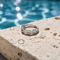 Clicker Wave in Oro Bianco al Pool Anello in oro bianco con cristalli su superficie di pietra, davanti a una piscina