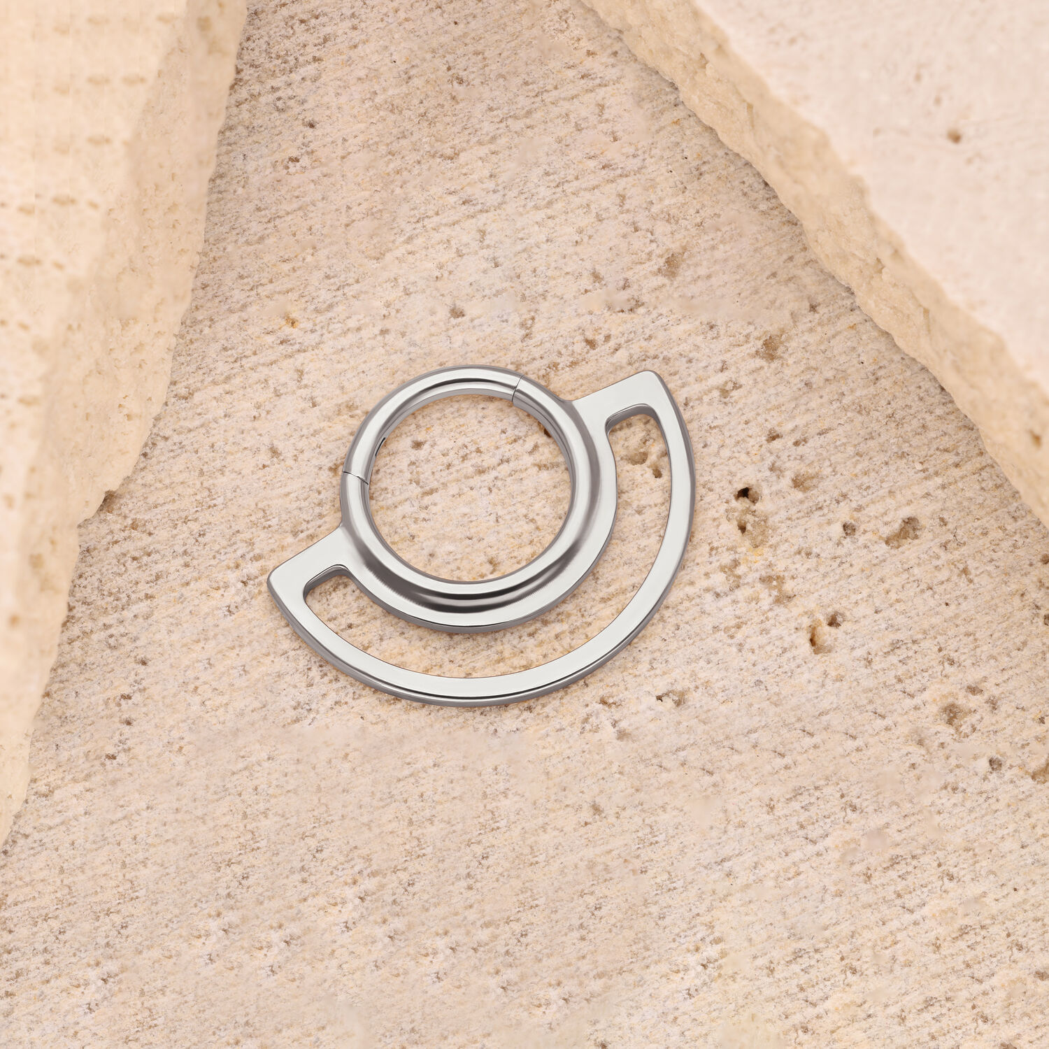 Clicker a Doppio Anello in Argento su Pietra Clicker ad anello in argento su sfondo di pietra beige, design circolare