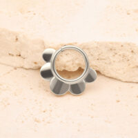 Clicker Half Flower in argento di titanio Clicker Half Flower in argento davanti a una pietra beige su sfondo chiaro