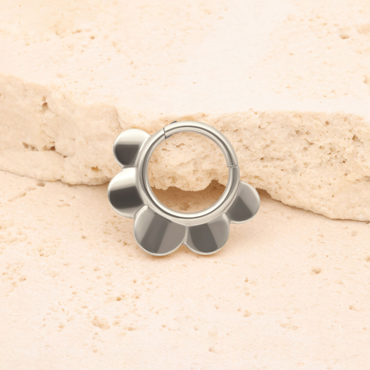 Clicker Half Flower in argento di titanio Clicker Half Flower in argento davanti a una pietra beige su sfondo chiaro