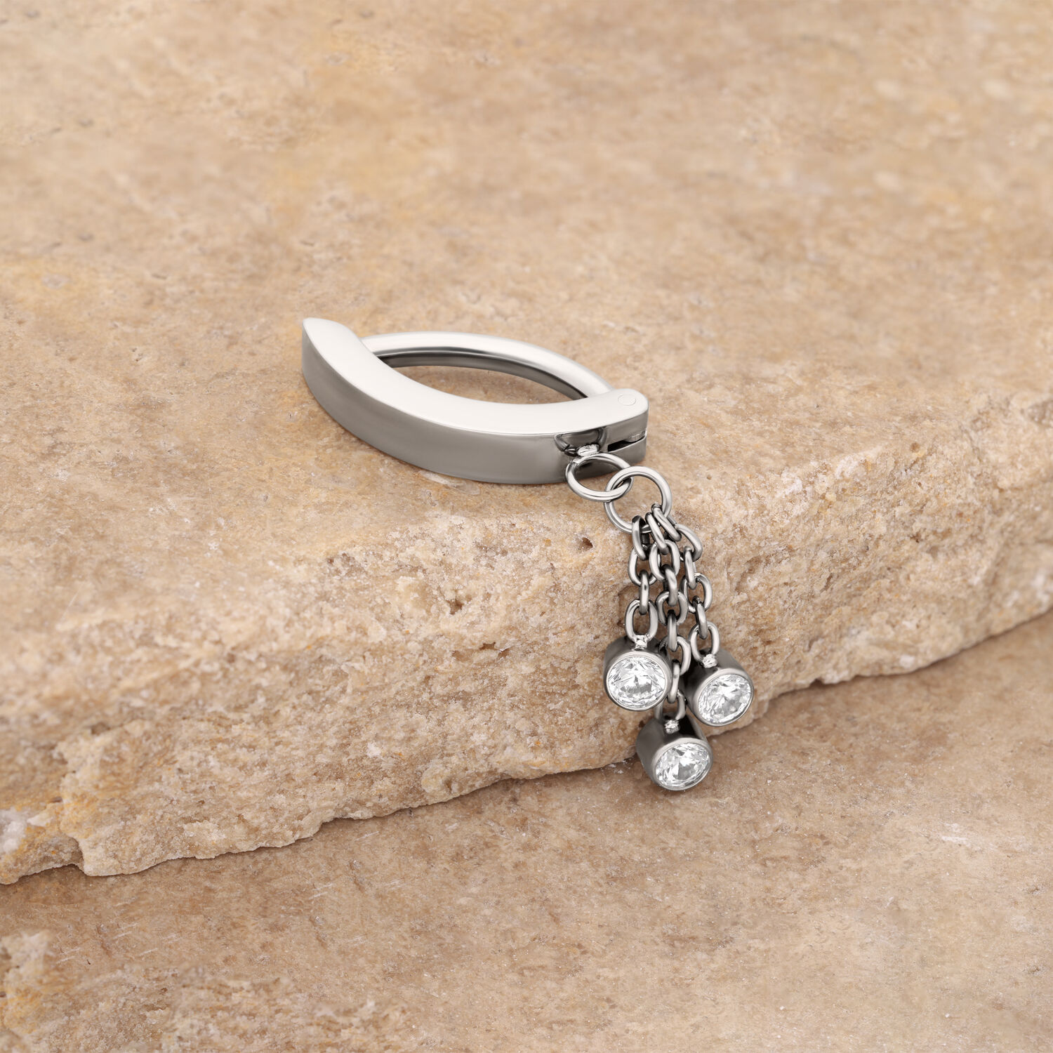 Clicker per ombelico in argento con pendente di cristallo Clicker per ombelico in argento con pendenti cristallini, posizionato su una pietra beige