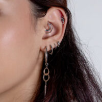 Orecchini a foro in argento con pendente Primo piano di un orecchio con diversi piercing in argento, tra cui un grande pendente e piccoli cerchi su sfondo bianco