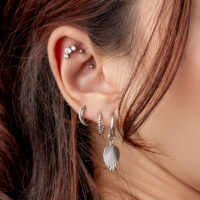 Piercing all'orecchio in argento con cristalli Primo piano di un orecchio con diversi piercing in argento e cristalli, capelli sullo sfondo