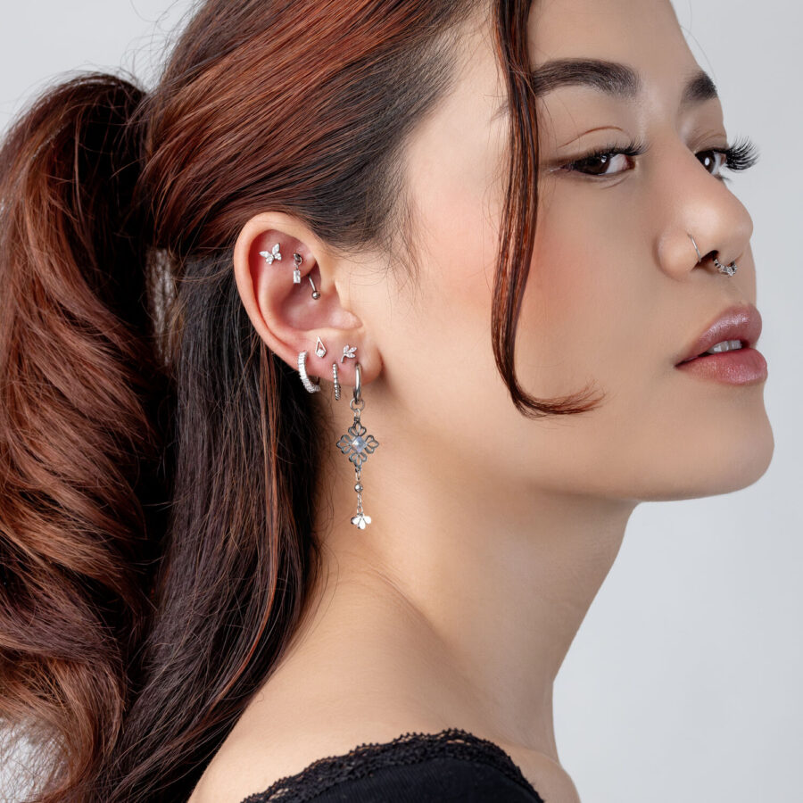 Donna con diversi accessori piercing d'argento all'orecchio, profilo laterale su sfondo grigio