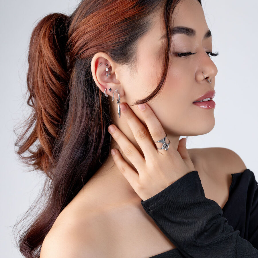 Donna con diversi piercing in argento e una maglia nera su sfondo bianco