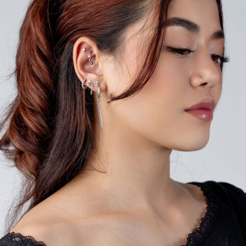 Donna con diversi piercing all'orecchio in argento di vari design, vista laterale