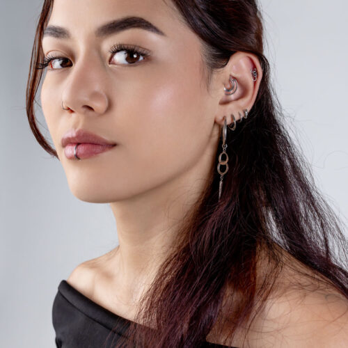 Donna con un clicker a doppio anello nell'orecchio e diversi piercing, su sfondo grigio