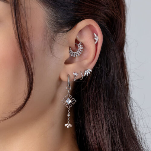 Primo piano di un orecchio con diversi piercing in argento e cristalli.