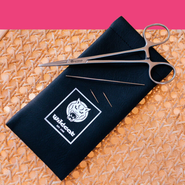 Kit piercing con pinza in acciaio e aghi su custodia nera su sfondo intrecciato