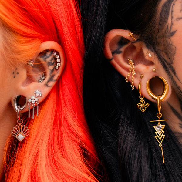 Due orecchie con piercing multipli, orecchini in acciaio e oro su capelli arancioni e neri