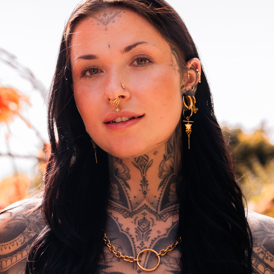 Donna con capelli neri, tatuaggi e gioielli in ottone, sfondo naturale
