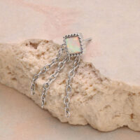 Anello in argento con pietra opale rettangolare e tre catene su sfondo beige