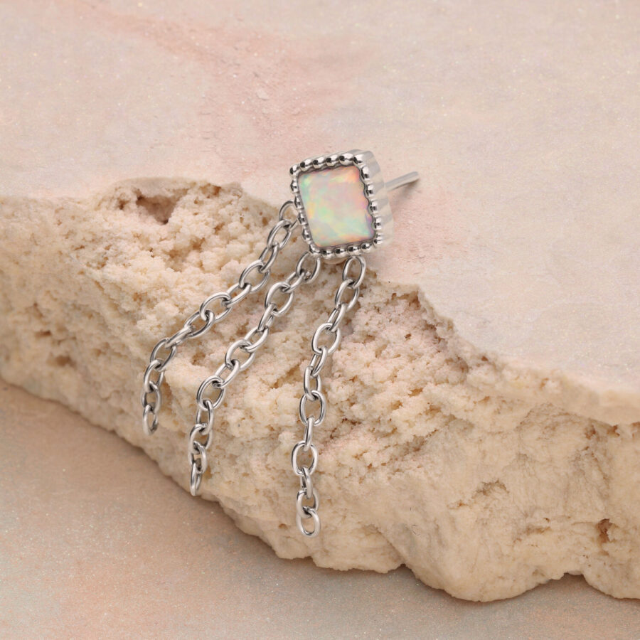 Anello in argento con pietra opale rettangolare e tre catene su sfondo beige