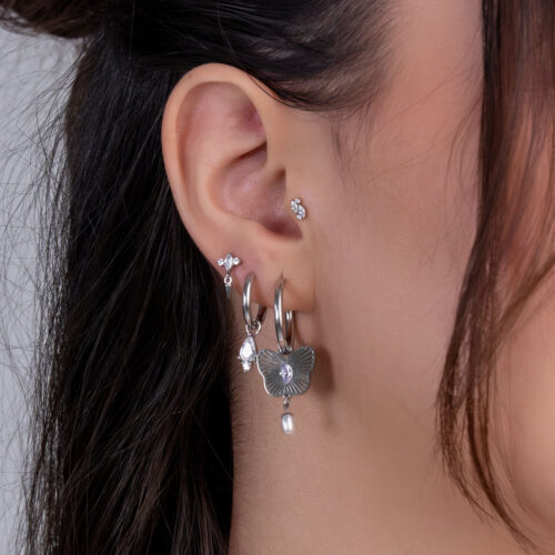 Primo piano di un orecchio con diversi piercing d'argento e cristalli chiari su sfondo chiaro