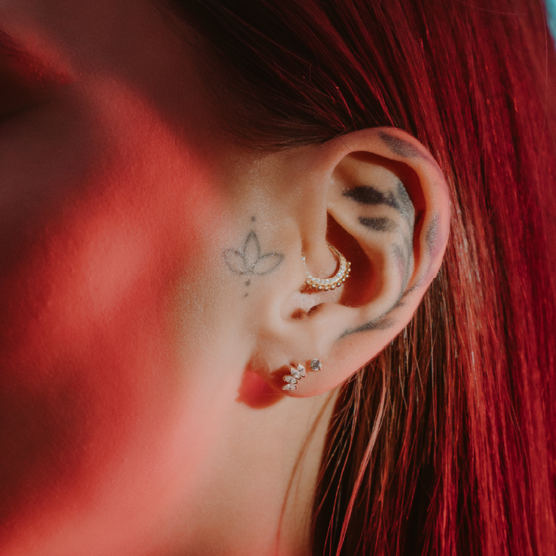 Orecchino a cerchio dorato su orecchio con capelli rossi e tattoo fiore stilizzato